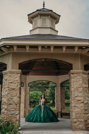 A majestic emerald ball gown photographed under a classic white gazebo with stone pillars.