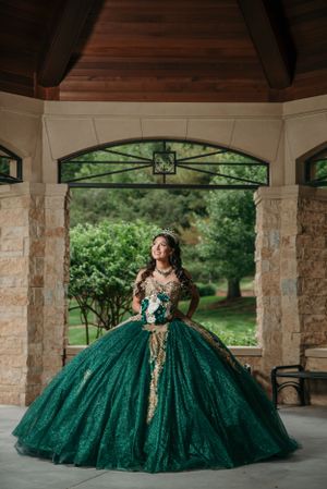 A stunning emerald green quinceañera dress with gold embellishments captured under an elegant pavilion.
