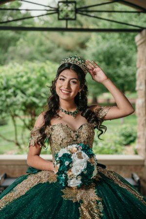 A joyful portrait in an emerald green ball gown with gold accents and matching crown under a pavilion.