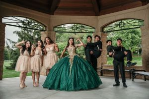 Wedding party in casual pose under outdoor gazebo with emerald green gown centerpiece.