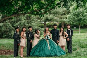 Group photo of a quinceañera celebration with attendants in pink dresses and black suits under a tree.