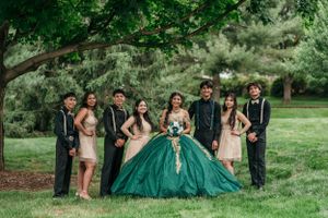 Quinceañera party group poses outdoors with matching formal attire in emerald green and blush pink.