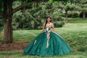Stunning emerald green ball gown with gold embellishments photographed in a garden setting.
