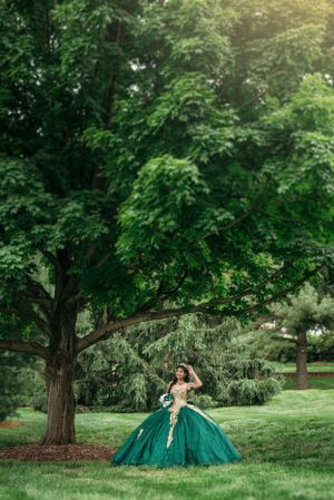 Dramatic outdoor portrait featuring an emerald green ball gown against lush garden scenery.
