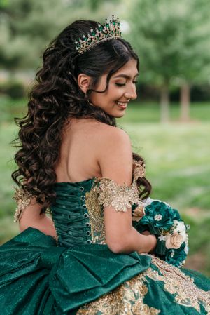 An ornate emerald and gold quinceanera dress with delicate lace-up back detail and tiara.