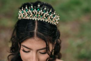 A sparkling tiara with emerald green stones crowns flowing dark curls.