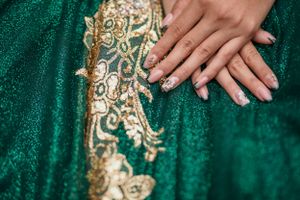 Detailed shot of gold embroidery on emerald green fabric with manicured hands.