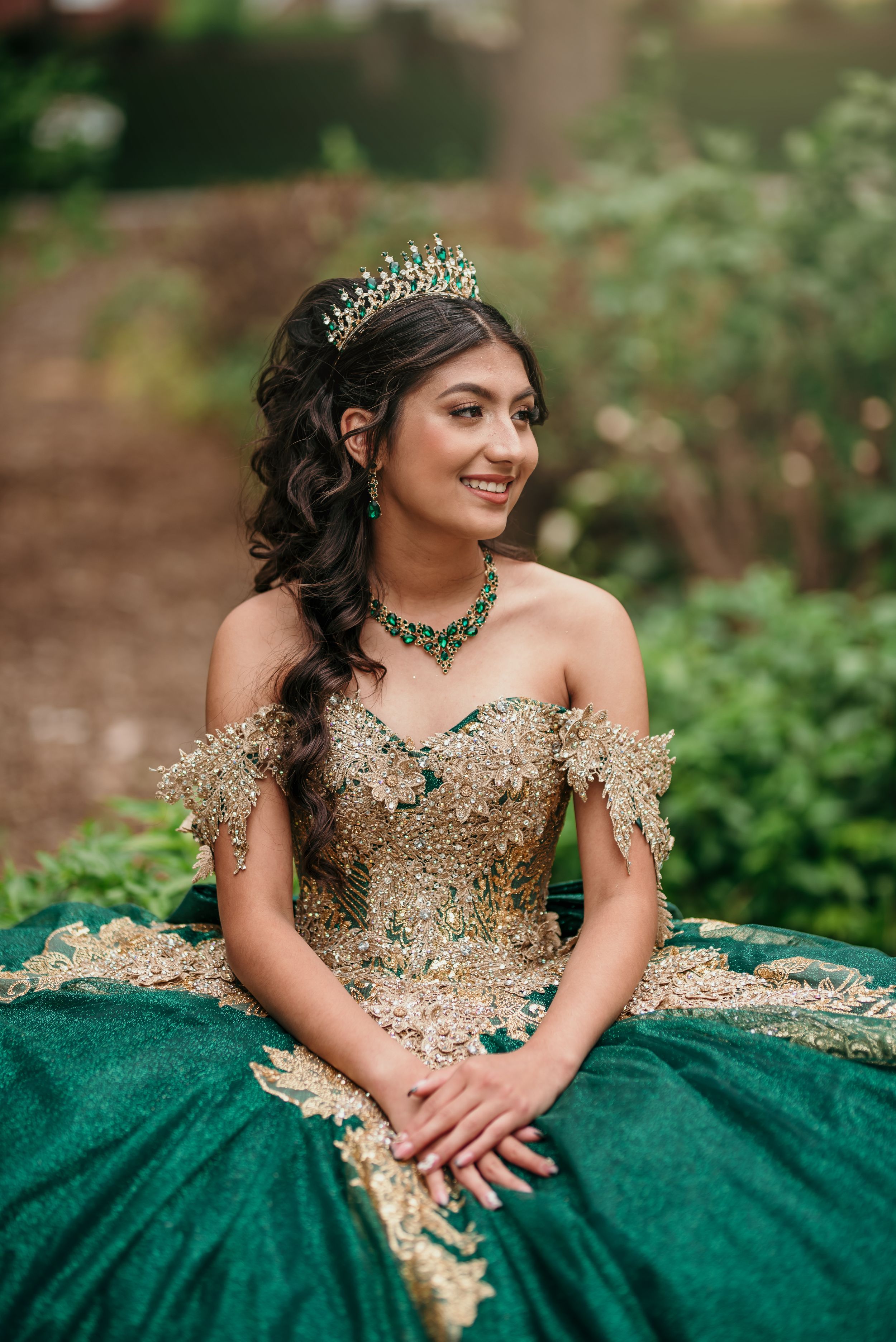 A stunning emerald and gold quinceañera dress with ornate details and a tiara creates an elegant portrait.
