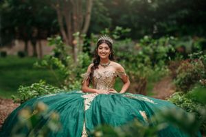 A stunning emerald green and gold quinceañera dress showcased in an outdoor garden setting.