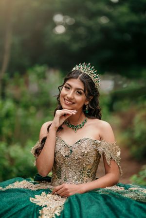An elegant portrait showcasing a sparkly gold and emerald green ball gown with matching accessories.