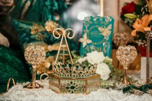 Gold crown and crystal decorations with emerald green accents for formal celebration.