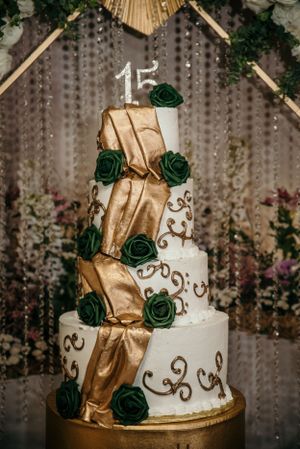 Elegant three-tier white and gold quinceañera cake decorated with emerald green roses and the number 15.