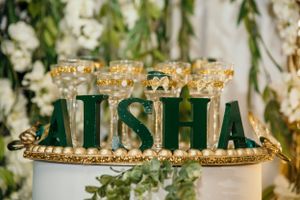 Emerald green decorative letters spelling AISHA with golden accents and crown details.