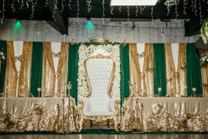 Elegant white throne chair setup with emerald green and gold reception backdrop and draping.