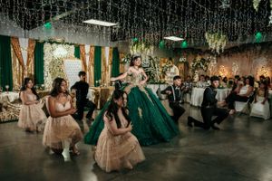 A celebration features dancers in elegant gowns performing at an event space decorated with hanging greenery.