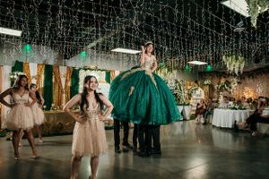 Quinceañera celebration in an elegant venue with emerald green ball gown and string lights.
