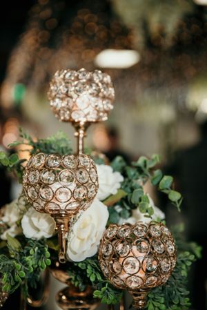 Elegant crystal and gold candle holders decorated with white roses and greenery.