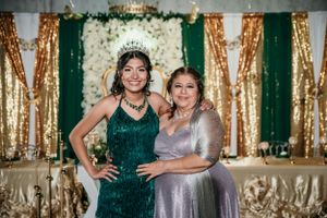 Two guests pose in front of an elegant green and gold backdrop at a formal event.
