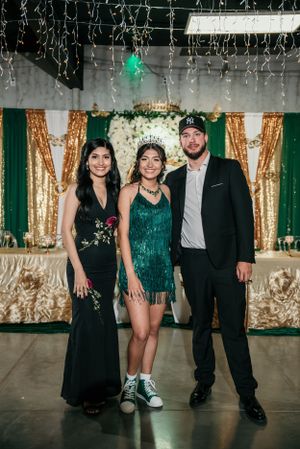 Three guests pose together in formal attire against gold and green backdrop at event.