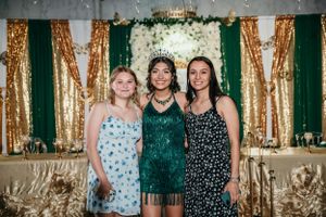 Three guests pose together against gold and green backdrop at formal event.