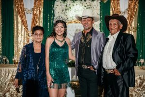 A group poses in formal attire against a backdrop with gold and green decor at a special celebration event.