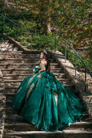 Dramatic photo of emerald ball gown on stone steps surrounded by autumn foliage.