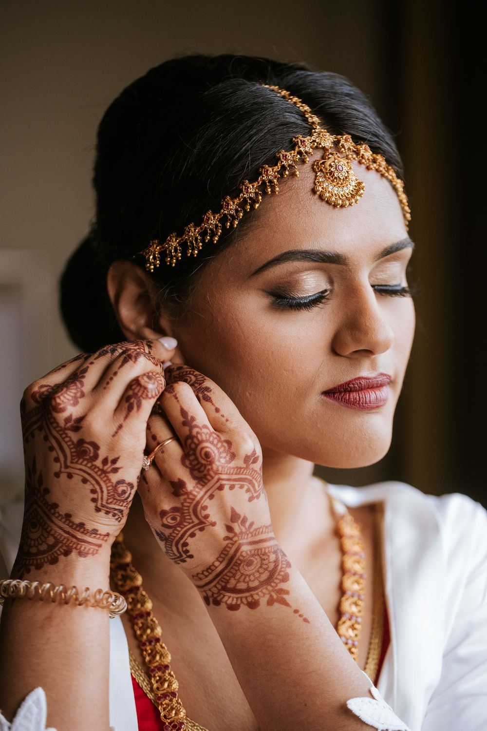 Close-up details of intricate henna designs and gold jewelry on hands during traditional Indian wedding preparations.