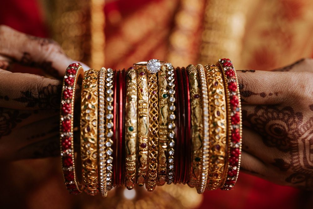 Collection of ornate gold and red bangles stacked together in traditional Indian bridal style.