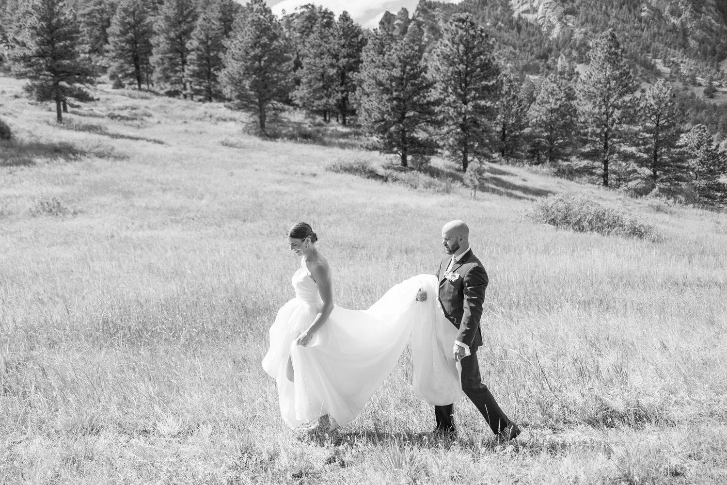 A couple walks hand in hand through a scenic wooded mountain path during a romantic outdoor photoshoot.