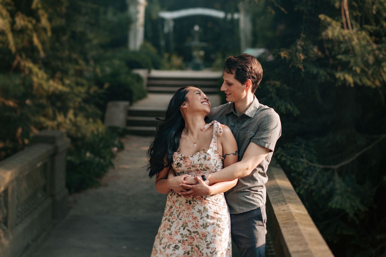 Romantic couple embraces during outdoor engagement photo session in a garden setting at sunset.