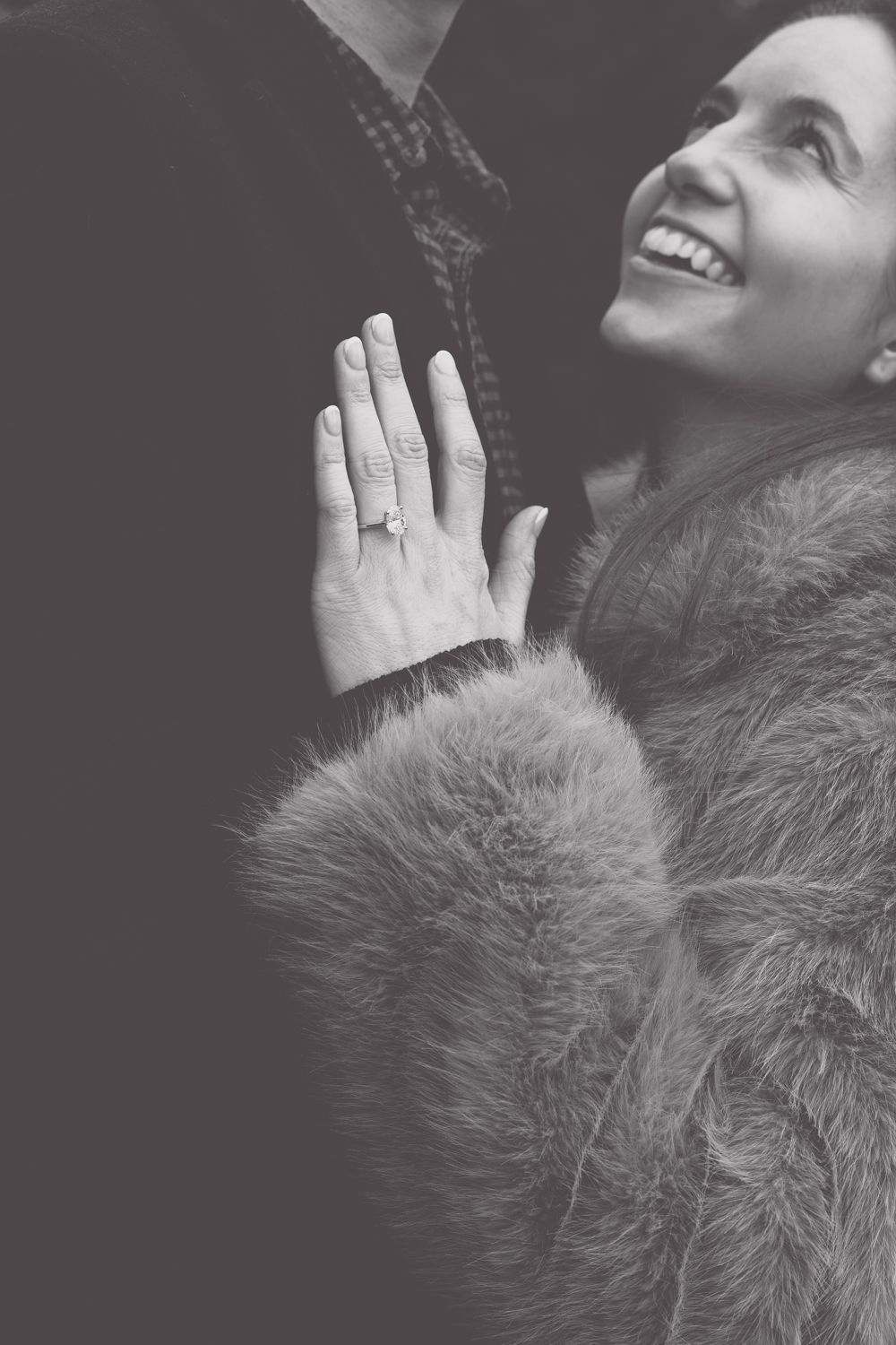 Black and white portrait of someone smiling while wearing a fuzzy fur coat and holding their hands together in prayer.