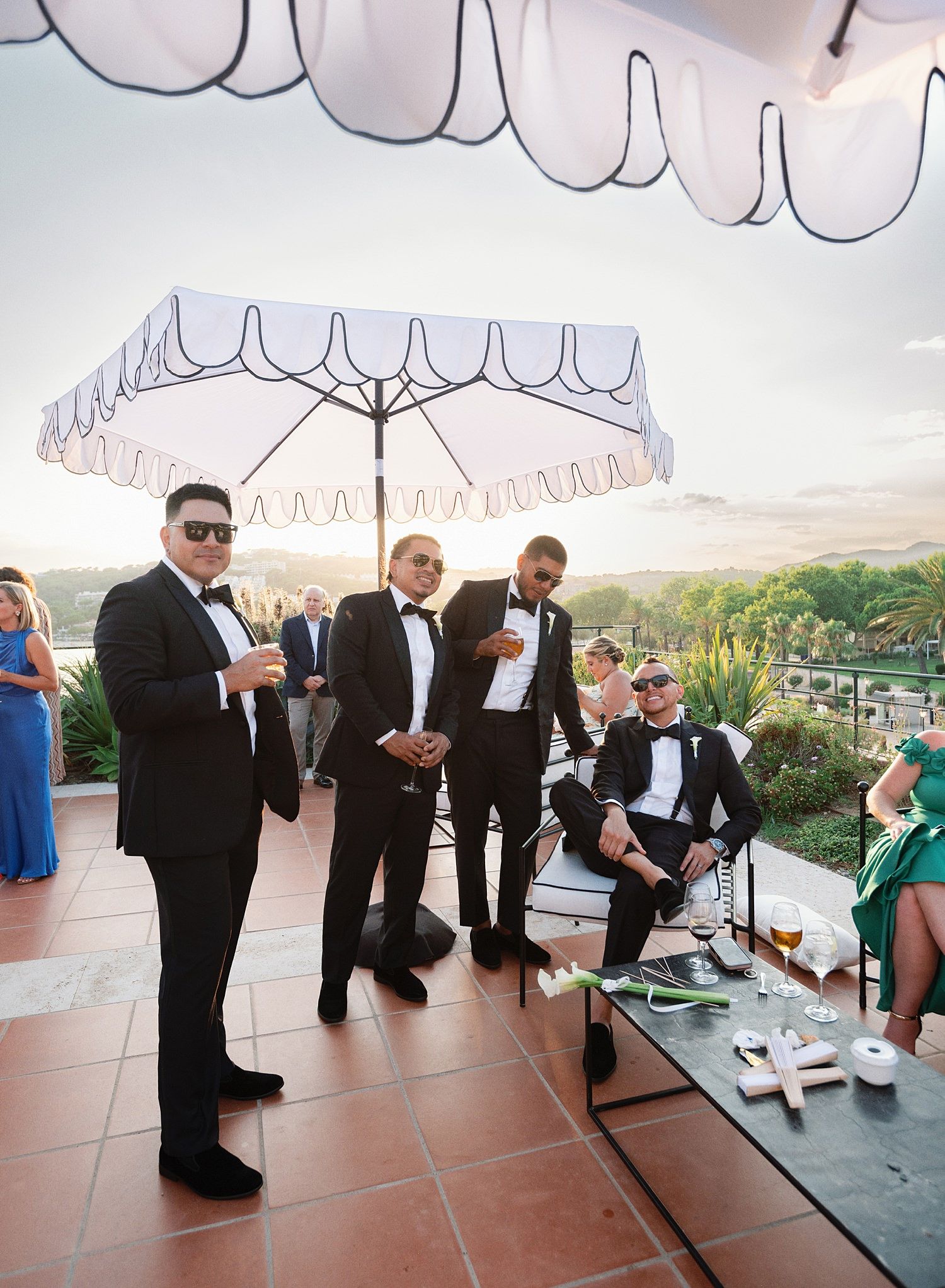 Wedding guests gather on an outdoor terrace under white umbrellas during a reception celebration.