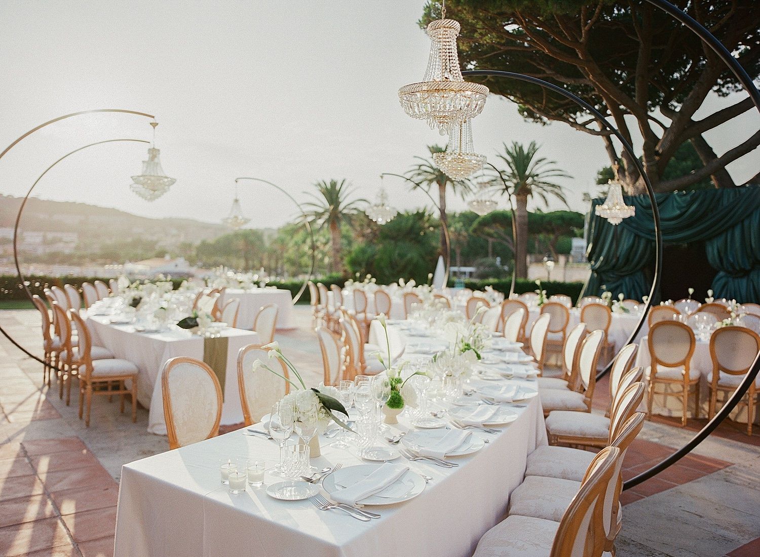 Elegant wedding reception setup with long tables, white linens, and wooden chairs in a bright indoor-outdoor venue.