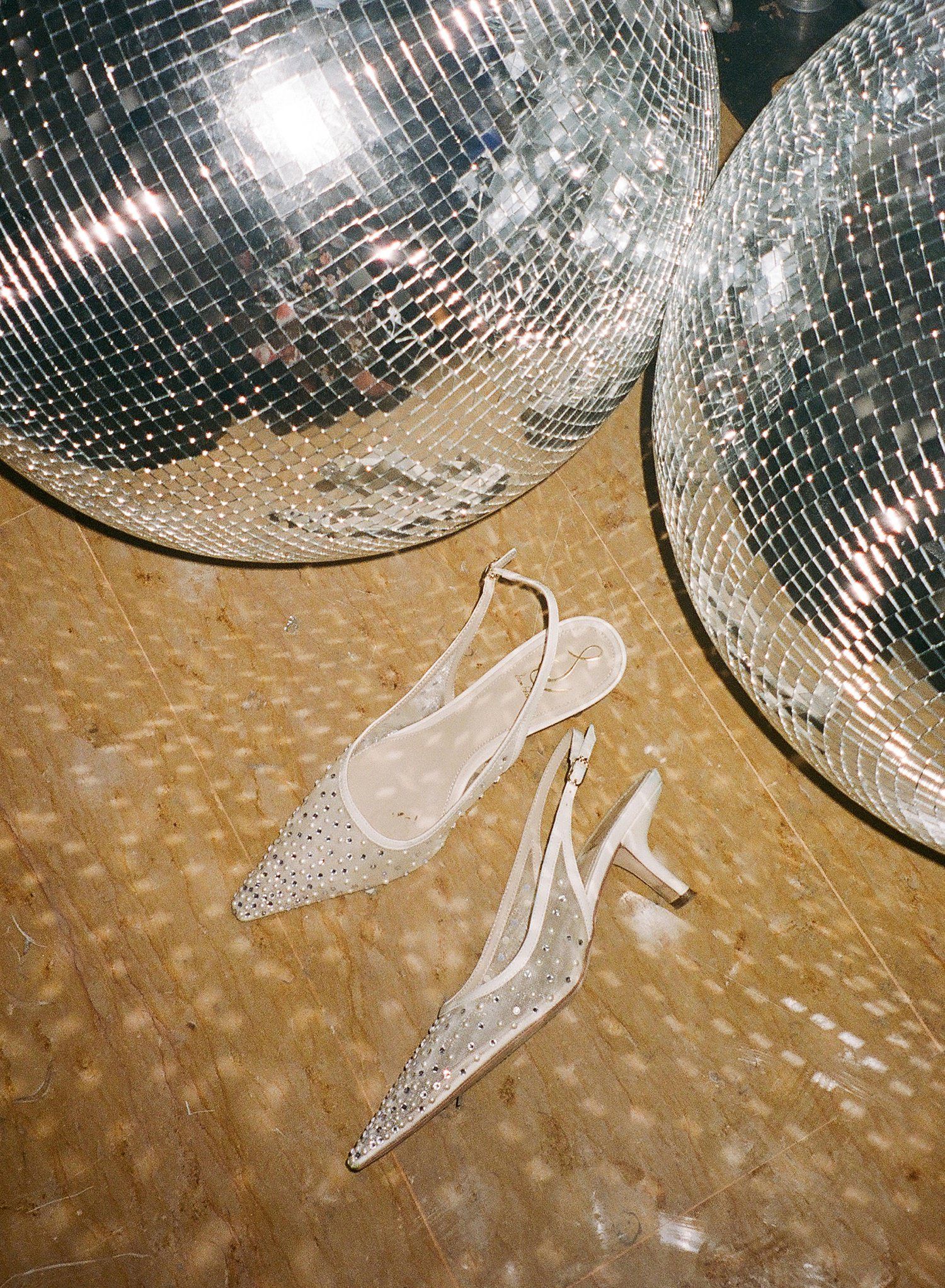 Shimmering disco balls reflect light patterns on a beige textured floor with a broken champagne glass below.