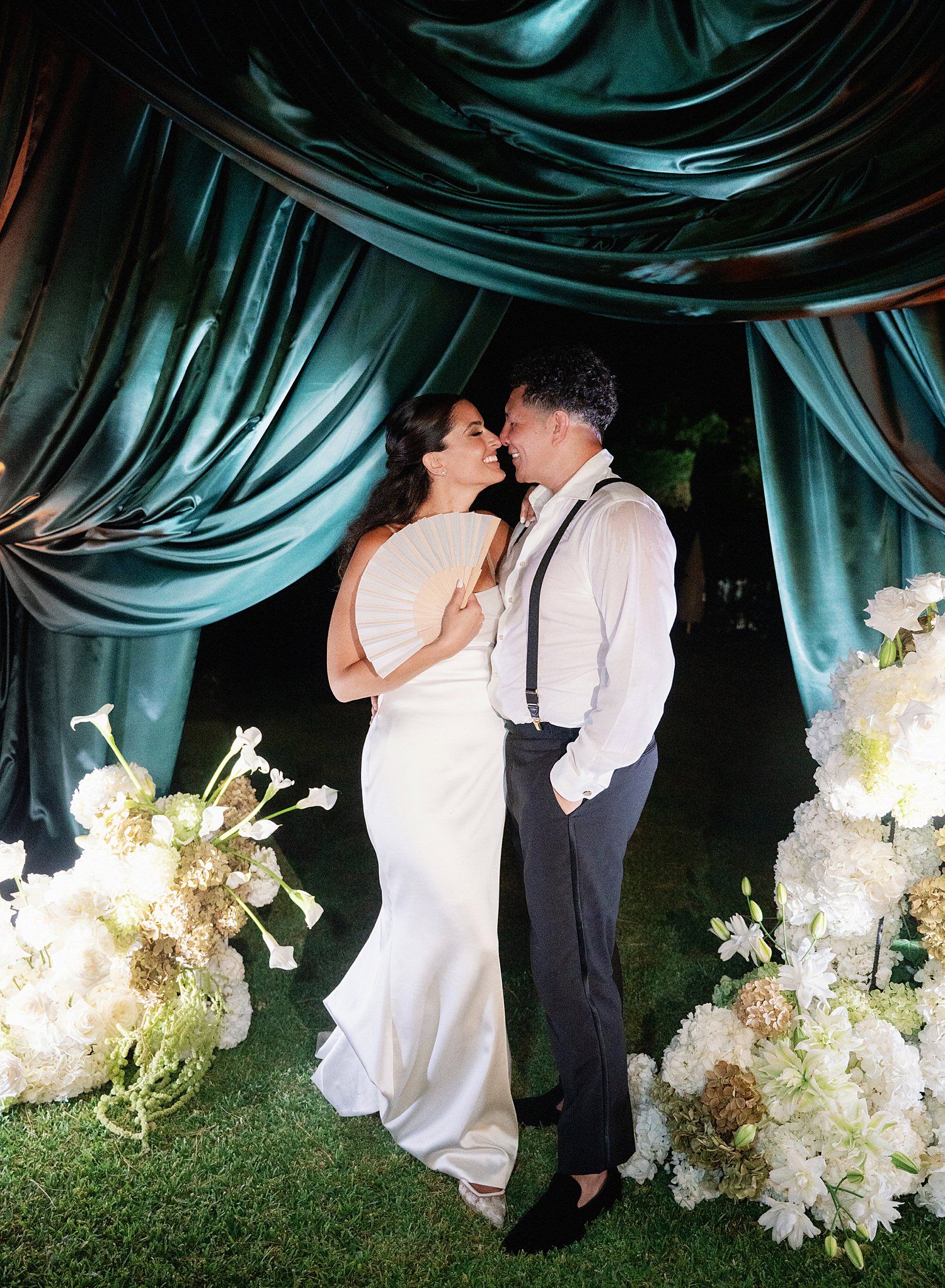 Romantic wedding couple shares intimate moments in sequence against dramatic blue draped backdrop with white floral arrangements.