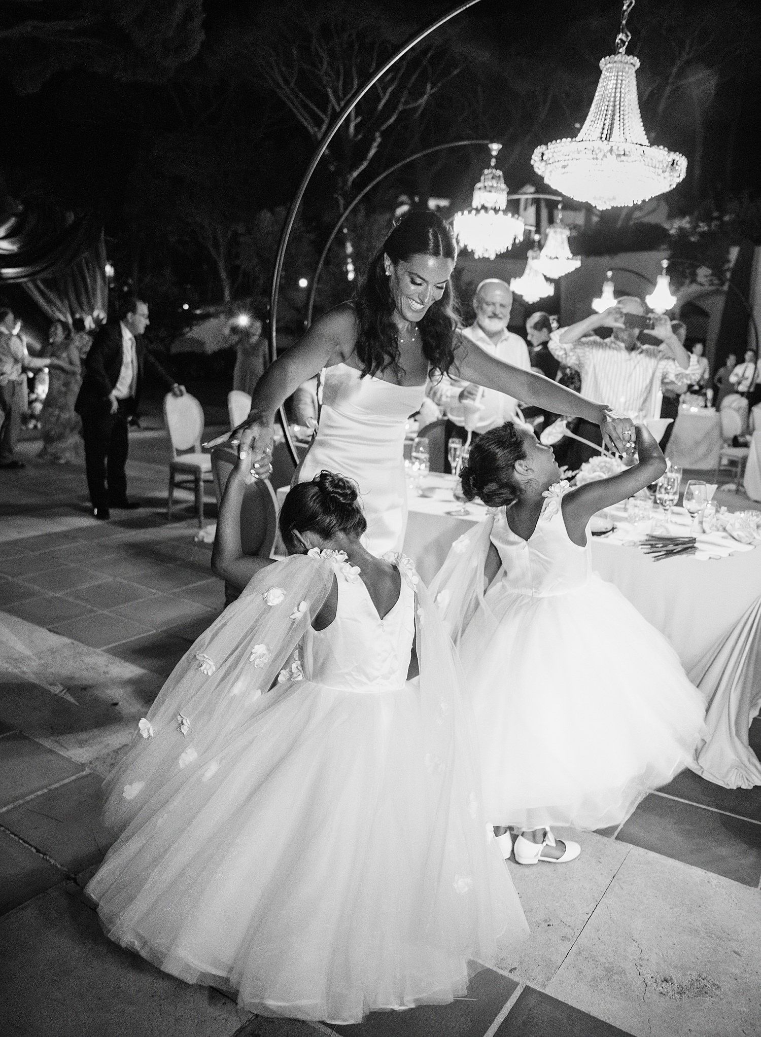 Elegant dancers in white tulle dresses twirl gracefully under crystal chandeliers at a formal ballroom event.