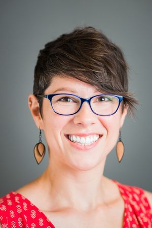 Casual portraits showing bright smile with blue glasses and wooden earrings in red patterned top.