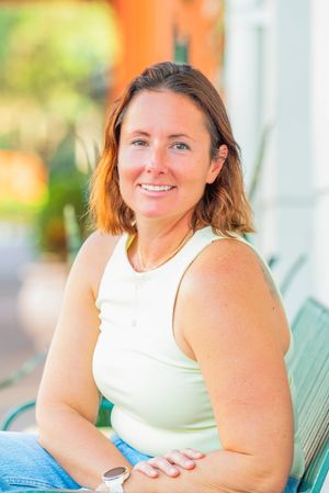 Smiling woman with auburn hair wearing a light green tank top, seated outdoors in a relaxed pose.