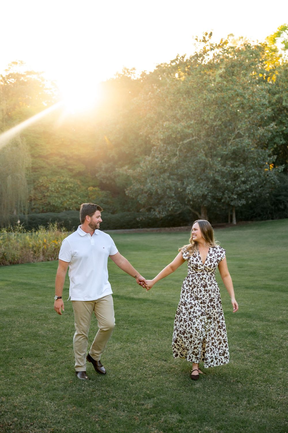 Couple dancing and holding hands in a sunlit field during golden hour.