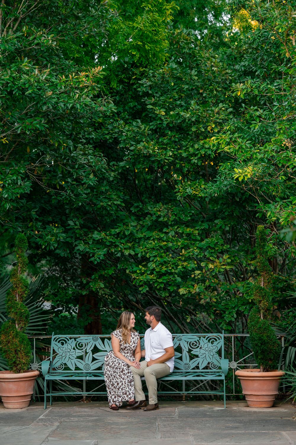 Couple sitting close together on a decorative teal garden bench surrounded by greenery.