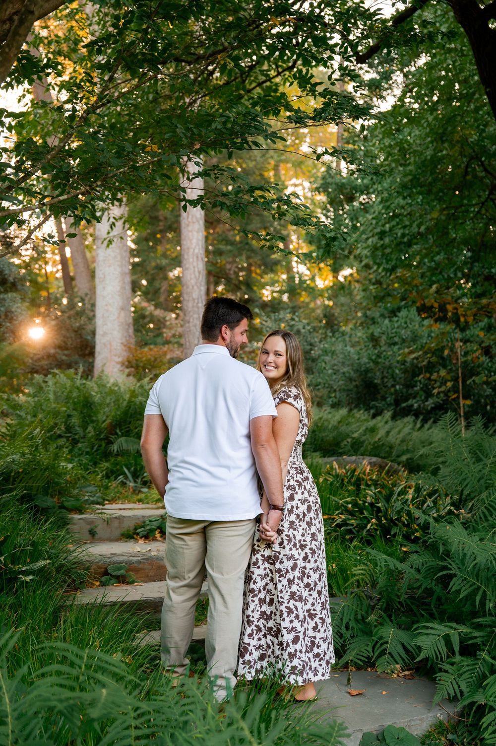 Couple walking through a garden path surrounded by tall trees and ferns.
