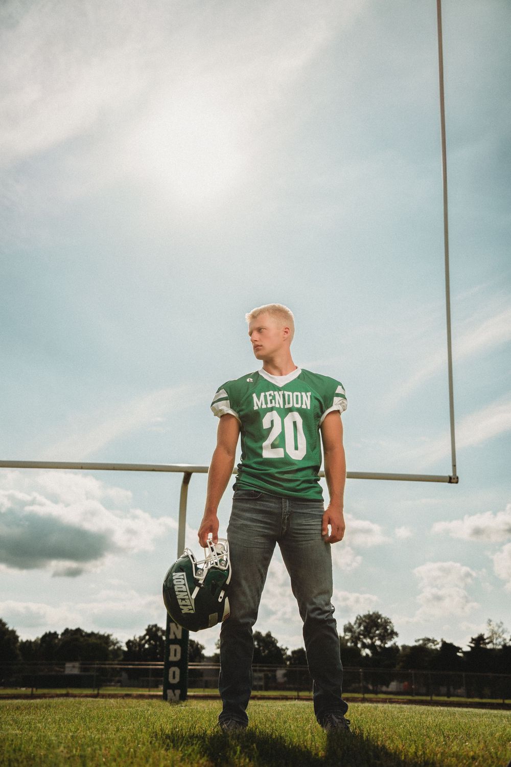 Male high school senior in Mendon football jersey number 20 posing at goal post.