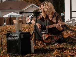 Musical equipment and instruments scattered among fallen autumn leaves outdoors.