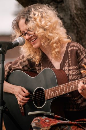 Musician playing acoustic guitar while wearing a brown plaid sweater in an intimate performance setting.