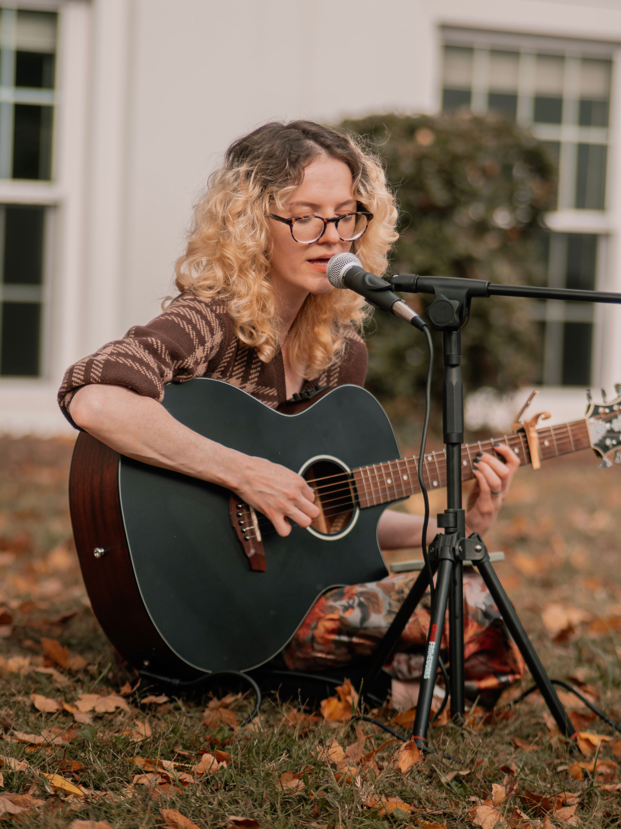 Acoustic guitarist sitting on autumn leaves with a microphone setup outdoors.
