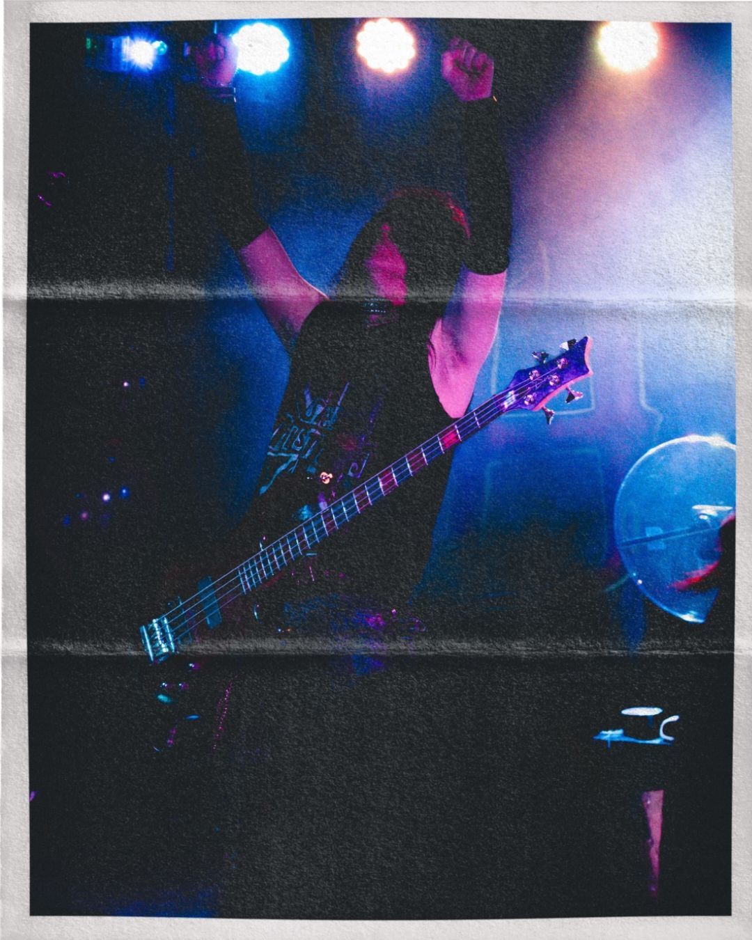 Electric bass guitar silhouetted against blue and pink stage lighting during a live performance.
