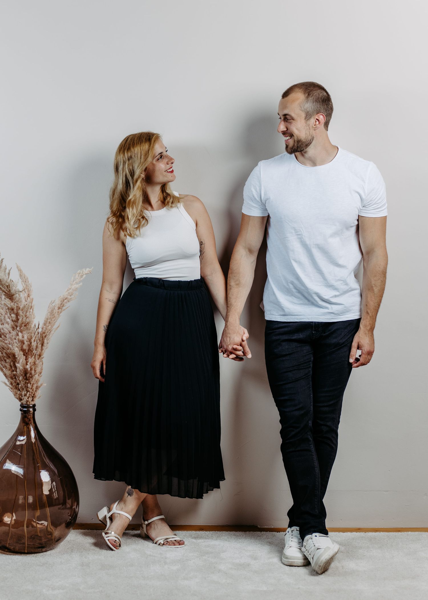 Couple in matching black and white outfits standing beside a vase with dried pampas grass in a minimalist setting.