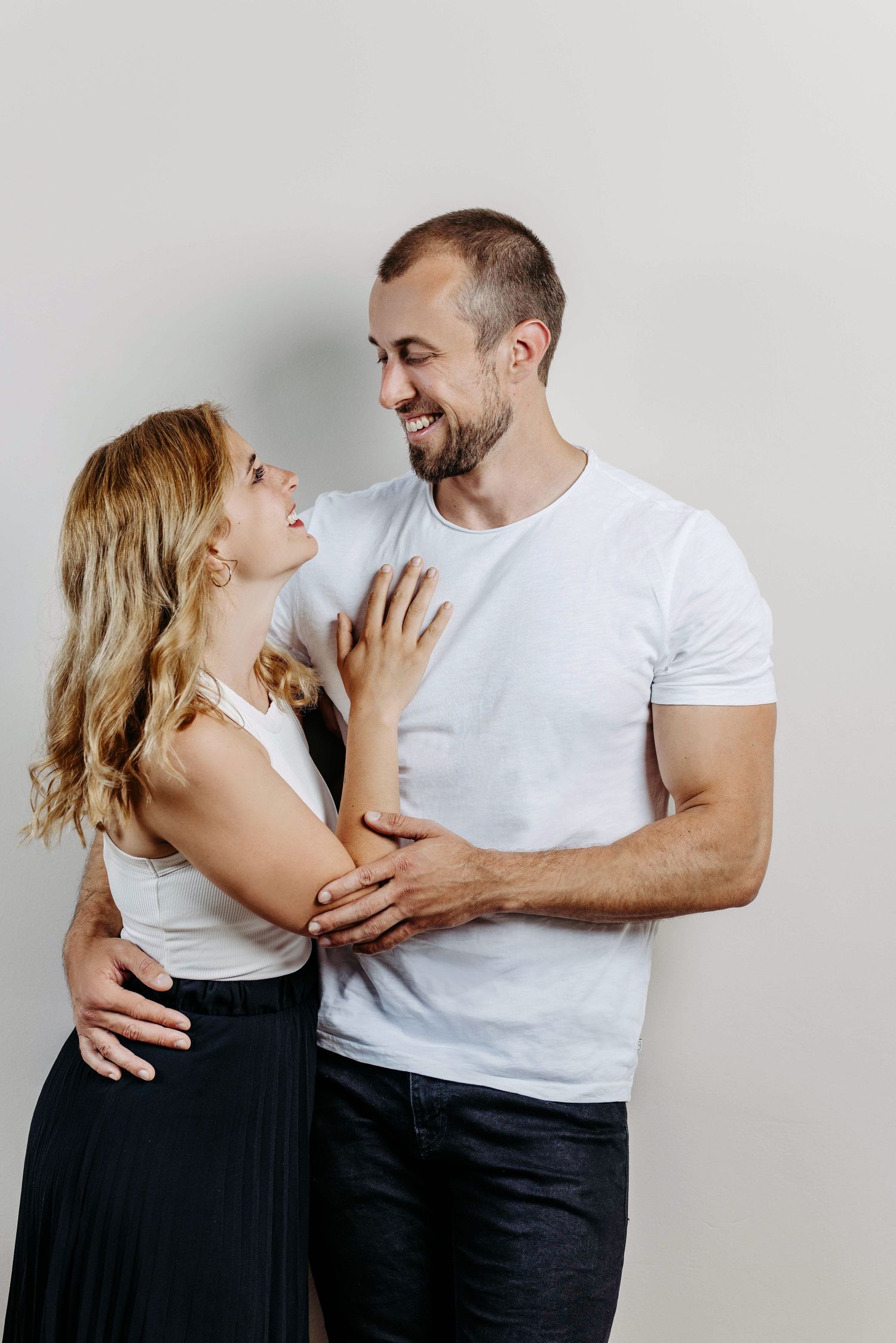 A couple in matching white shirts and black pants share intimate moments in a minimalist photo series against a light background.