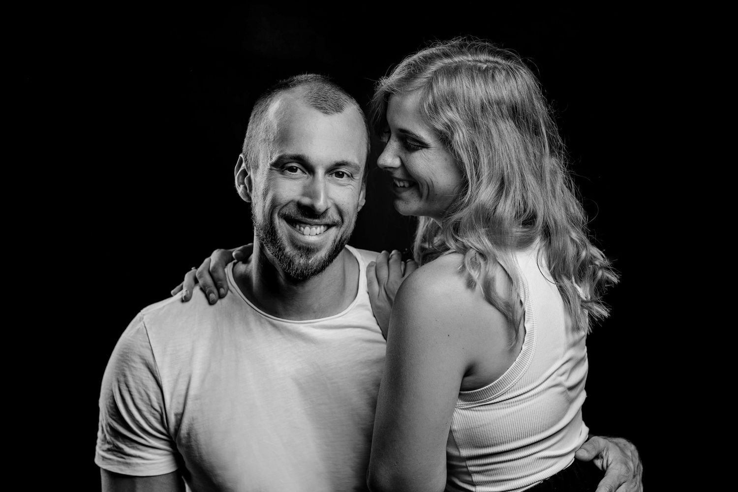 A romantic black and white portrait of a couple in casual attire sharing an intimate moment together.