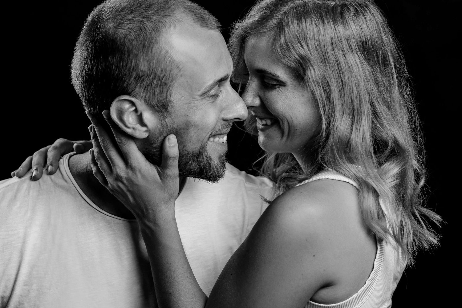 An affectionate black and white photograph showing a tender moment between a couple in close embrace.